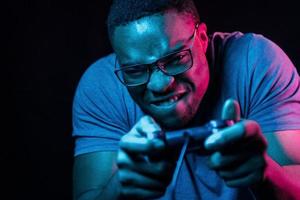 joue au jeu en utilisant le contrôleur. éclairage néon futuriste. jeune homme afro-américain dans le studio photo