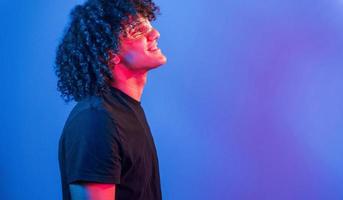 dans des verres futuristes. jeune bel homme aux cheveux bouclés est à l'intérieur dans le studio avec éclairage au néon photo