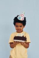 heureux petit enfant afro-américain s'amuser à l'intérieur à la fête d'anniversaire détient un gâteau photo
