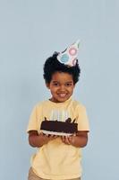 heureux petit enfant afro-américain s'amuser à l'intérieur à la fête d'anniversaire détient un gâteau photo