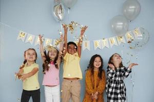 ballons et confettis. les enfants célébrant la fête d'anniversaire à l'intérieur s'amusent ensemble photo