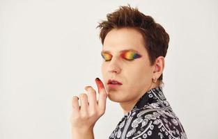 jeune homme gay est debout dans le studio et pose pour un appareil photo. maquillage multicolore sur les doigts du visage photo