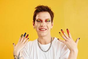 jeune homme gay est debout dans le studio et pose pour un appareil photo. maquillage arc-en-ciel photo