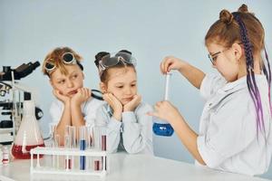 des enfants en blouse blanche jouent un scientifique en laboratoire en utilisant un équipement photo