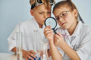 des enfants en blouse blanche jouent un scientifique en laboratoire en utilisant un équipement photo