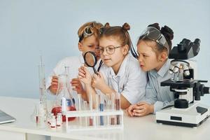 des enfants en blouse blanche jouent un scientifique en laboratoire en utilisant un équipement photo