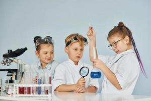 des enfants en blouse blanche jouent un scientifique en laboratoire en utilisant un équipement photo