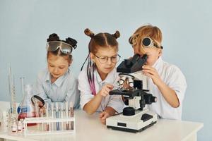 à l'aide d'un microscope. des enfants en blouse blanche jouent un scientifique en laboratoire en utilisant un équipement photo