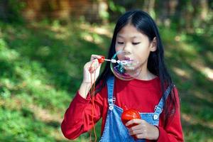 fille asiatique soufflant des bulles de savon jouant à l'extérieur dans le parc. jeu de concept, jouets, activités de loisirs pour enfants. mise au point douce et sélective. photo