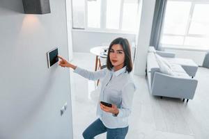 utilise une tablette fixée au mur. la jeune femme est à l'intérieur dans la chambre de la maison intelligente pendant la journée photo