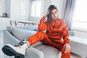 posant pour une caméra en costume rouge. jeune femme est à l'intérieur dans la chambre d'une maison moderne pendant la journée photo