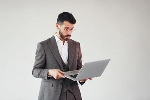 avec un ordinateur portable dans les mains. jeune homme d'affaires élégant en costume à l'intérieur. conception du succès photo