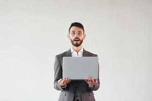 avec un ordinateur portable dans les mains. jeune homme d'affaires élégant en costume à l'intérieur. conception du succès photo