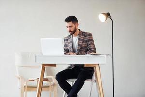 utilise un ordinateur portable. jeune homme d'affaires élégant en costume à l'intérieur. conception du succès photo