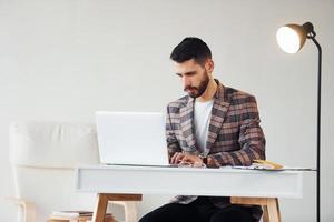 utilise un ordinateur portable. jeune homme d'affaires élégant en costume à l'intérieur. conception du succès photo