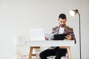 utilise un ordinateur portable. jeune homme d'affaires élégant en costume à l'intérieur. conception du succès photo