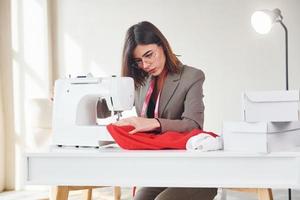 couturière travaille avec du tissu rouge. jeune femme en vêtements formels est à l'intérieur. conception du style photo