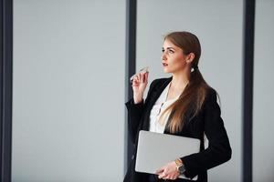 debout sur fond gris. jeune femme adulte en vêtements formels est à l'intérieur au bureau photo