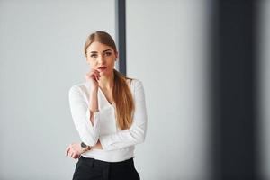 debout sur fond gris. jeune femme adulte en vêtements formels est à l'intérieur au bureau photo