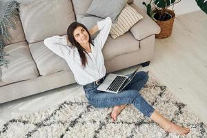 avec ordinateur portable. belle jeune femme en jeans et chemise blanche est à la maison photo