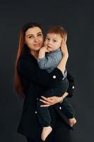 mère en vêtements noirs élégants est avec son petit fils dans le studio photo