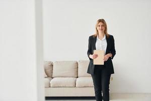 femme en vêtements formels debout près d'un canapé à l'intérieur contre un mur blanc photo