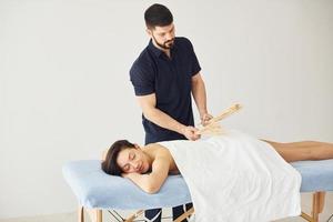 guy utilise des bâtons spéciaux. jeune femme est allongée quand un homme fait un massage de son corps au spa photo