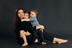 femme en vêtements élégants noirs est avec son petit fils et sa fille dans le studio photo