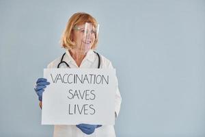 la vaccination sauve la bannière des vies. femme médecin senior en blouse blanche se tient à l'intérieur photo