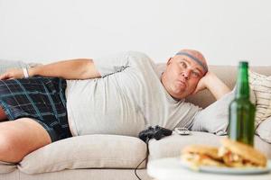 hamburgers et bière. homme allongé sur le canapé. drôle d'homme en surpoids dans des vêtements décontractés est à l'intérieur à la maison photo