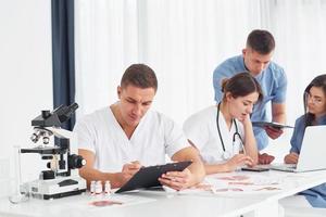 à l'aide d'un microscope. groupe de jeunes médecins travaille ensemble dans le bureau moderne photo