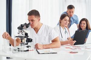 homme avec microscope. groupe de jeunes médecins travaille ensemble dans le bureau moderne photo