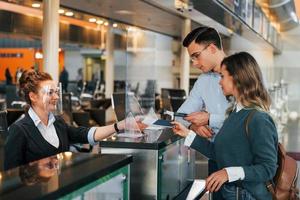 employé vérifiant les documents. jeune couple est à l'aéroport ensemble photo