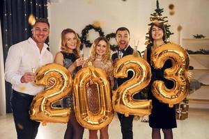 tenant des ballons avec le numéro 2023. un groupe de personnes organise une fête du nouvel an à l'intérieur photo
