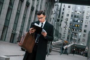 détenir des documents. homme d'affaires en costume noir et cravate est à l'extérieur de la ville photo