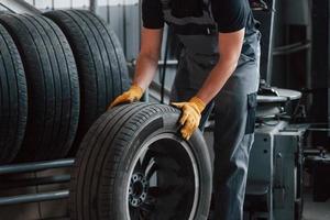 marcher avec un pneu. homme en uniforme travaille dans le service automobile photo