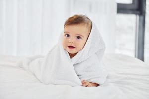 avec une serviette blanche. mignon petit bébé est à l'intérieur dans la chambre domestique photo