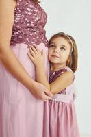 conception de l'anticipation. mère enceinte. femme en robe debout avec sa fille dans le studio avec un fond blanc photo