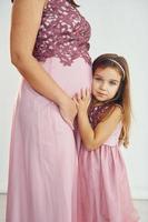 conception de l'anticipation. mère enceinte. femme en robe debout avec sa fille dans le studio avec un fond blanc photo