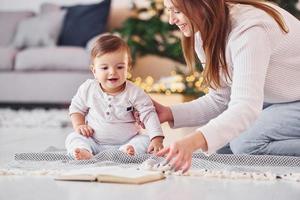 lire un livre ensemble. mère avec sa petite fille est à l'intérieur à la maison ensemble photo