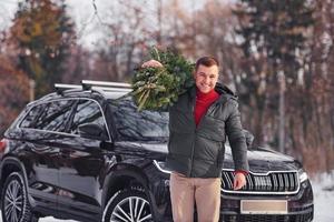 dans la foret. l'homme avec un petit sapin vert est à l'extérieur près de sa voiture. conception de vacances photo