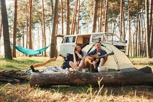 assis près de la tente. jeune couple voyage ensemble dans la forêt pendant la journée photo