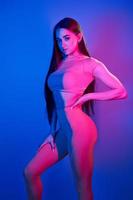 montre le corps. jeune femme à la mode debout dans le studio avec néon photo
