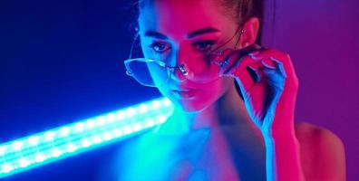 tient le bâton d'éclairage au néon. jeune femme à la mode debout dans le studio photo