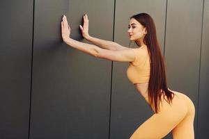 appuyé contre le mur. jeune femme en vêtements de sport a une séance de fitness à l'extérieur photo