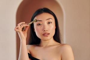 outil pour nettoyer la peau. jeune femme asiatique sérieuse debout à l'intérieur photo