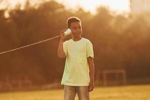 parler en utilisant une tasse sur le nœud. un enfant afro-américain s'amuse sur le terrain pendant la journée d'été photo