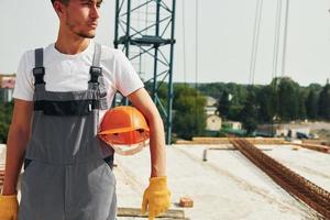 faire une pause. un jeune ouvrier du bâtiment en uniforme est occupé dans le bâtiment inachevé photo