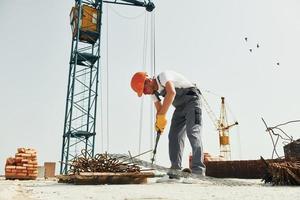 la grue est à l'arrière-plan. un jeune ouvrier du bâtiment en uniforme est occupé dans le bâtiment inachevé photo