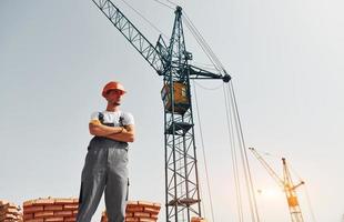 avec grue à l'arrière-plan. un jeune ouvrier du bâtiment en uniforme est occupé dans le bâtiment inachevé photo